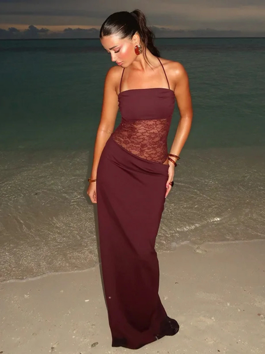 Woman in a burgundy evening gown standing on a beach with ocean in the background