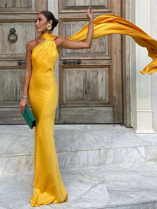 Woman in a yellow evening gown holding a flowing fabric against a marble floor and wooden door background.