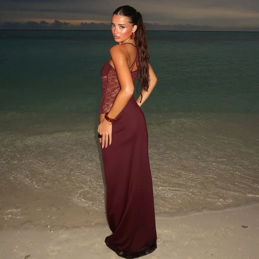 Woman in a burgundy evening gown standing on a beach at sunset.